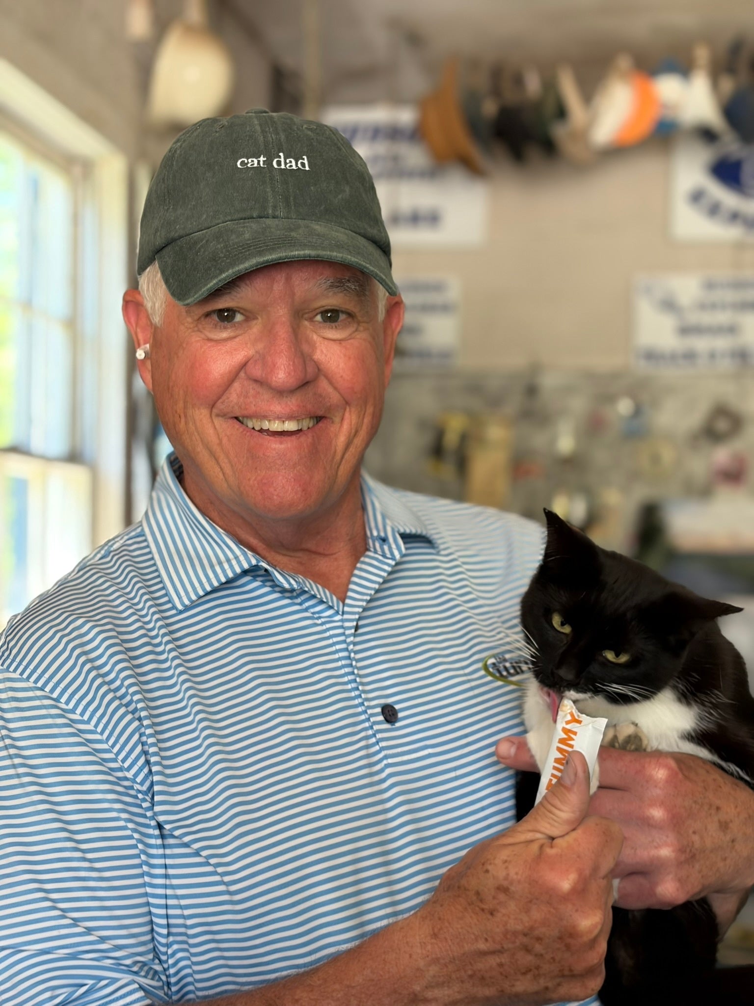 Cat dad in a Salty Cat Cat Dad Cap feeds his black and white cat—a must for cat lovers!.