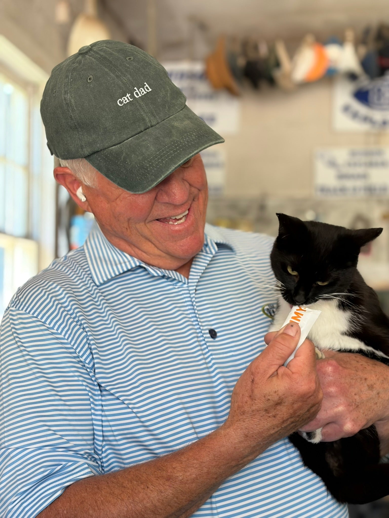 Smiling man in Salty Cat Cat Dad Cap gives treats to cat—ideal for Salty Cat fans and cat dads.